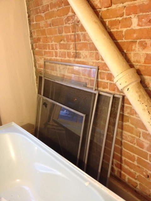 Bathroom Before: Storm window collection against exposed brick wall with waste pipe. This will become a solid wall where the tub and loo go.